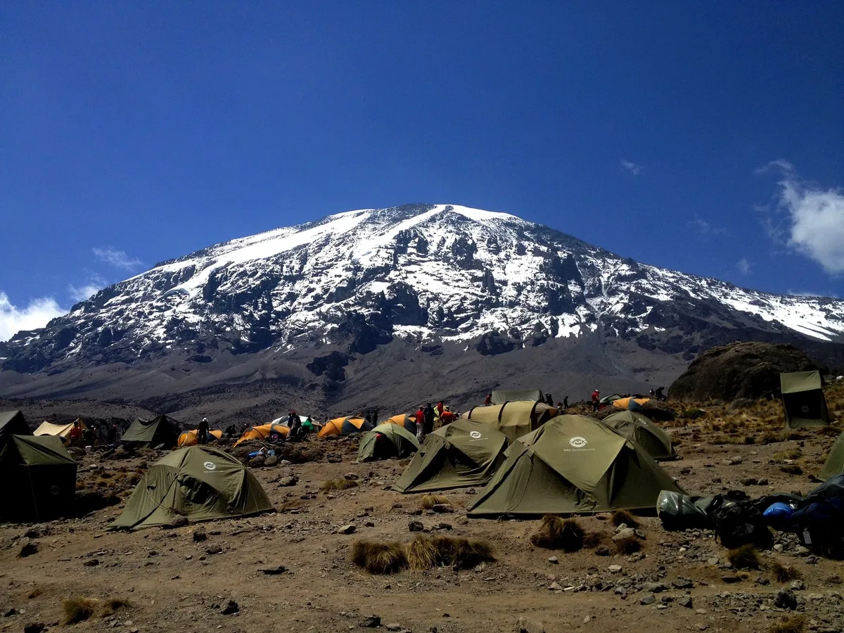 Tents pitched on the open alpine desert below the snow-capped dome of Kibo